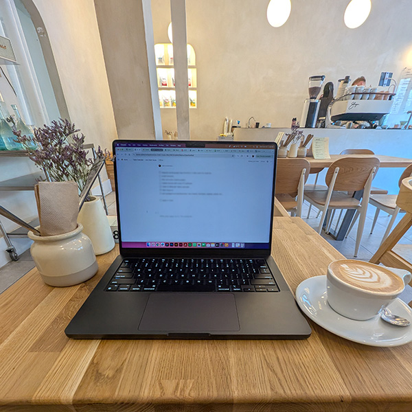 Laptop open on a wooden caf&eacute; table next to a latte, and a plant.