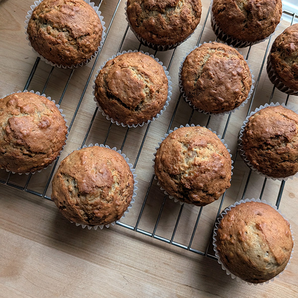 A dozen golden-brown muffins cooling on a wire rack.