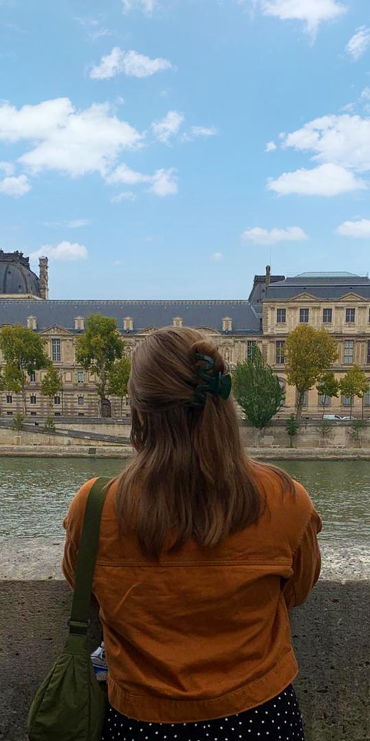 Hannah viewed from behind looking out over the Seine river towards the Louvre.
