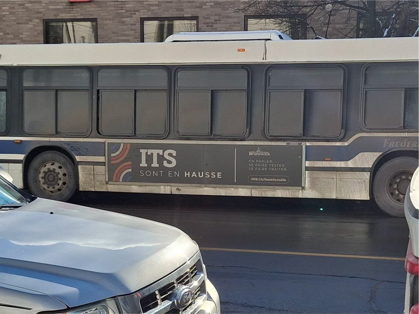 A real transit bus in winter conditions displaying the French-language 'ITS sont en hausse' ad, covered in road salt and slush.